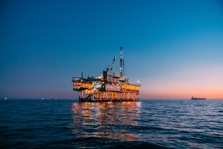Offshore oil and gas platform operating at sunset in the ocean.